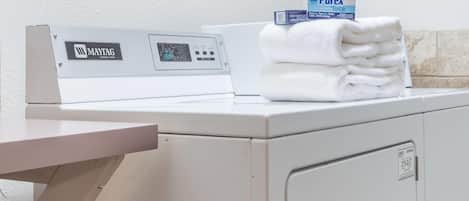 Una lavadora Maytag con un panel de control, una pila de toallas blancas y una caja de detergente Purex.