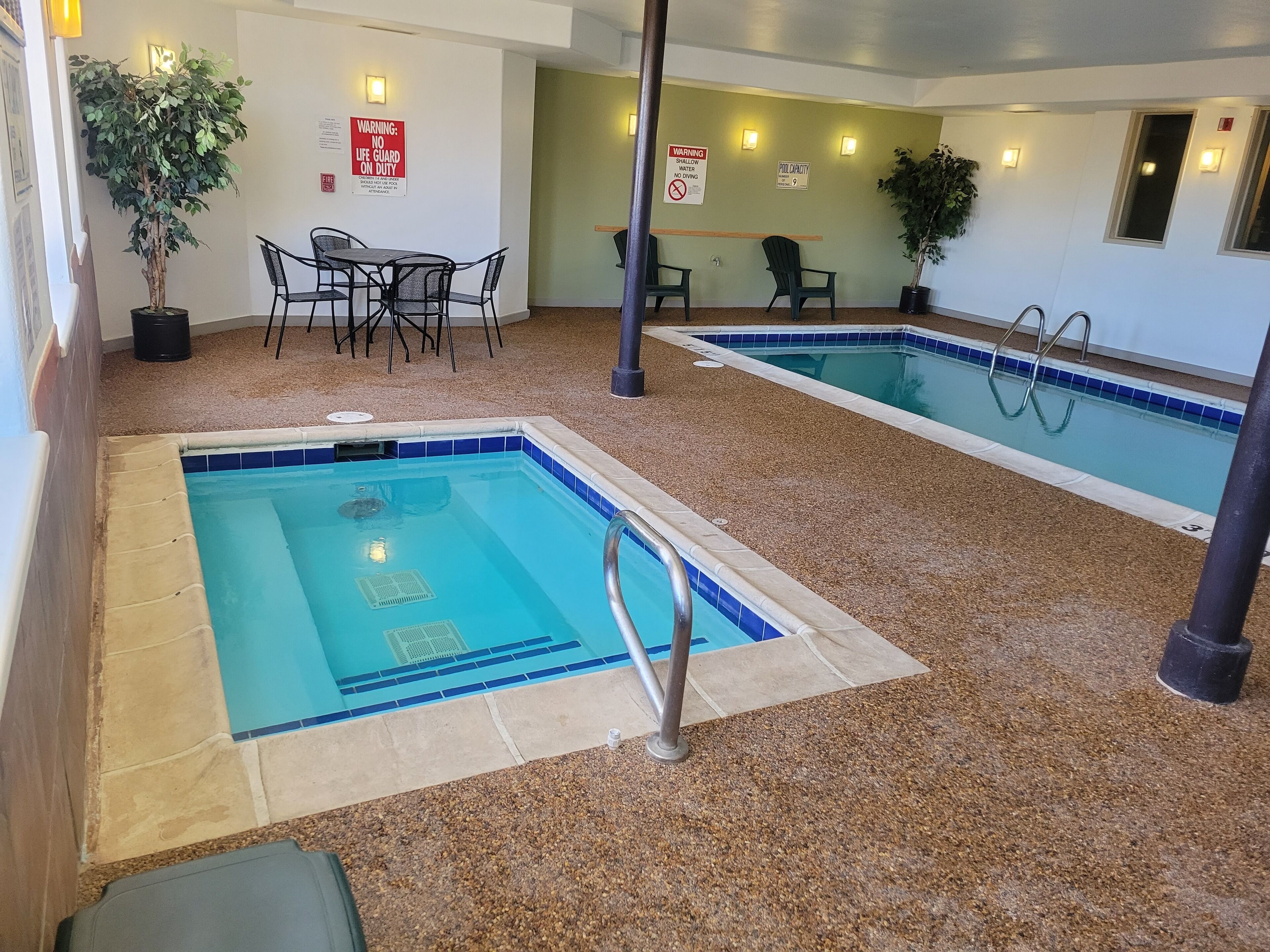 An indoor pool area with two pools, seating, and safety signs.