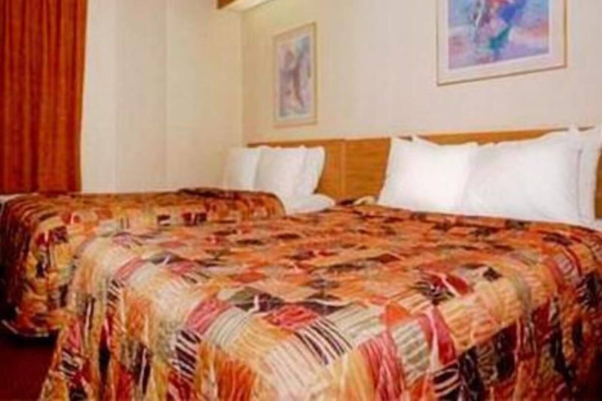 Ein Hotelzimmer mit zwei Betten, einem Holzkopfende, einem roten Vorhang und zwei gerahmten Bildern an der Wand.