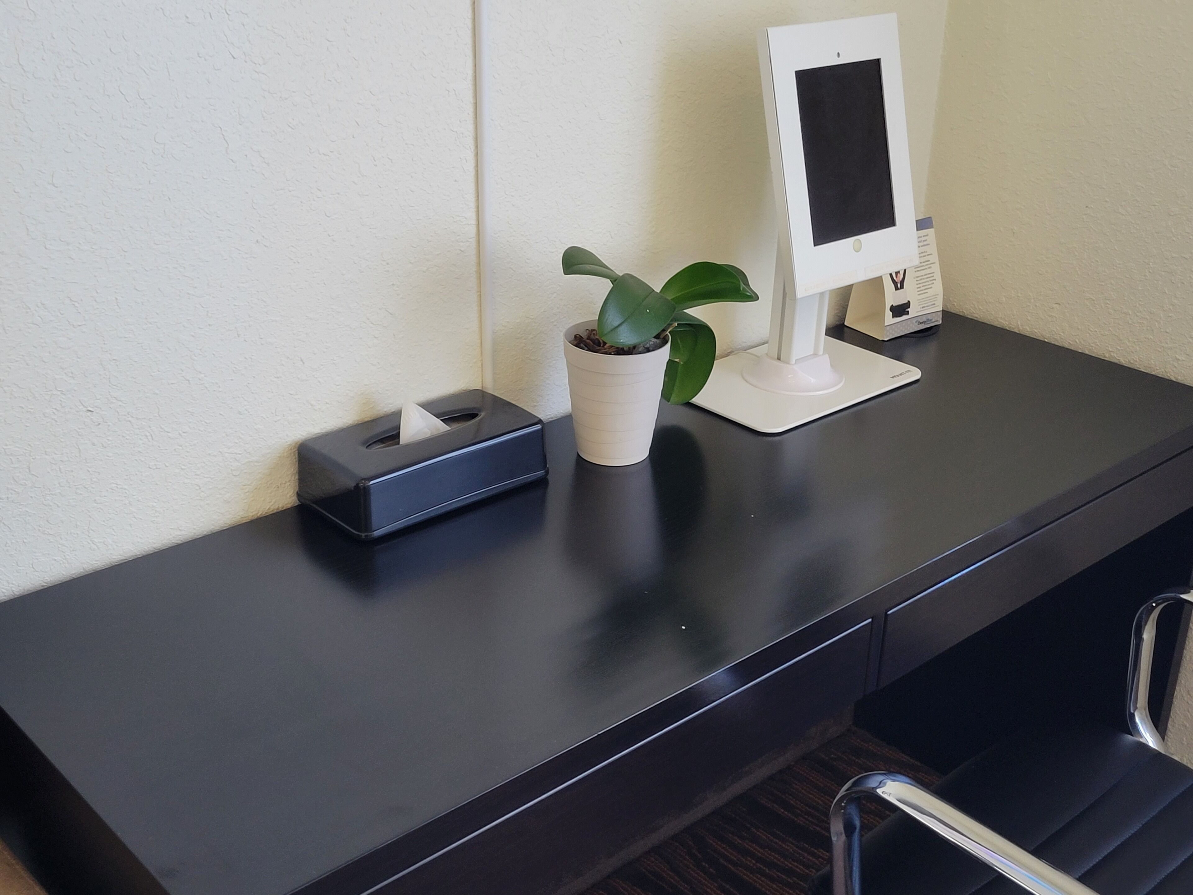 A desk with a tissue box, a potted plant, and a digital kiosk.