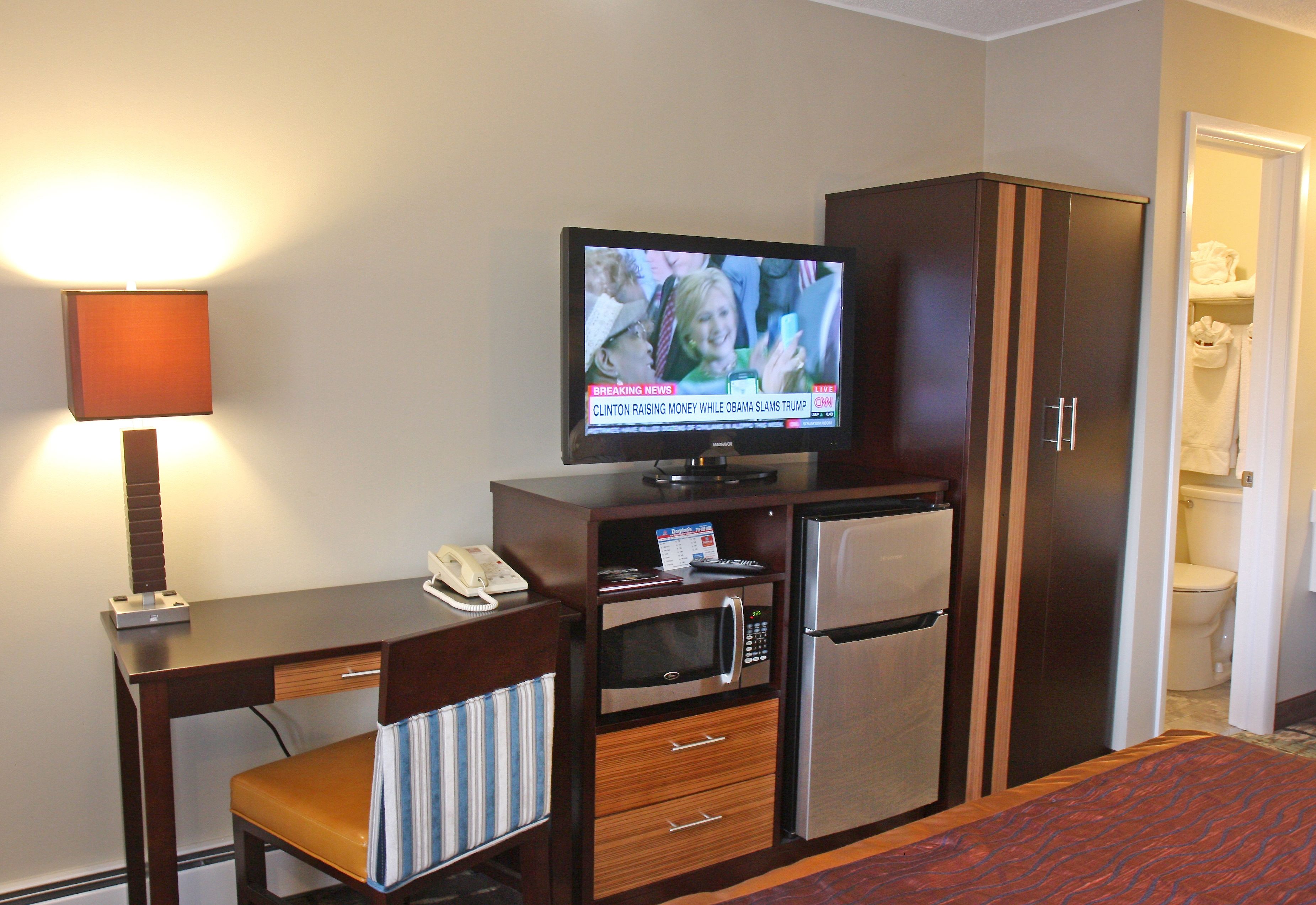 Ett hotellrum med ett skrivbord, en tv, en mikrovågsugn, ett kylskåp och en garderob.