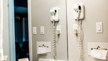 A hotel bathroom with a large mirror, a sink, a hairdryer, and a towel rack.