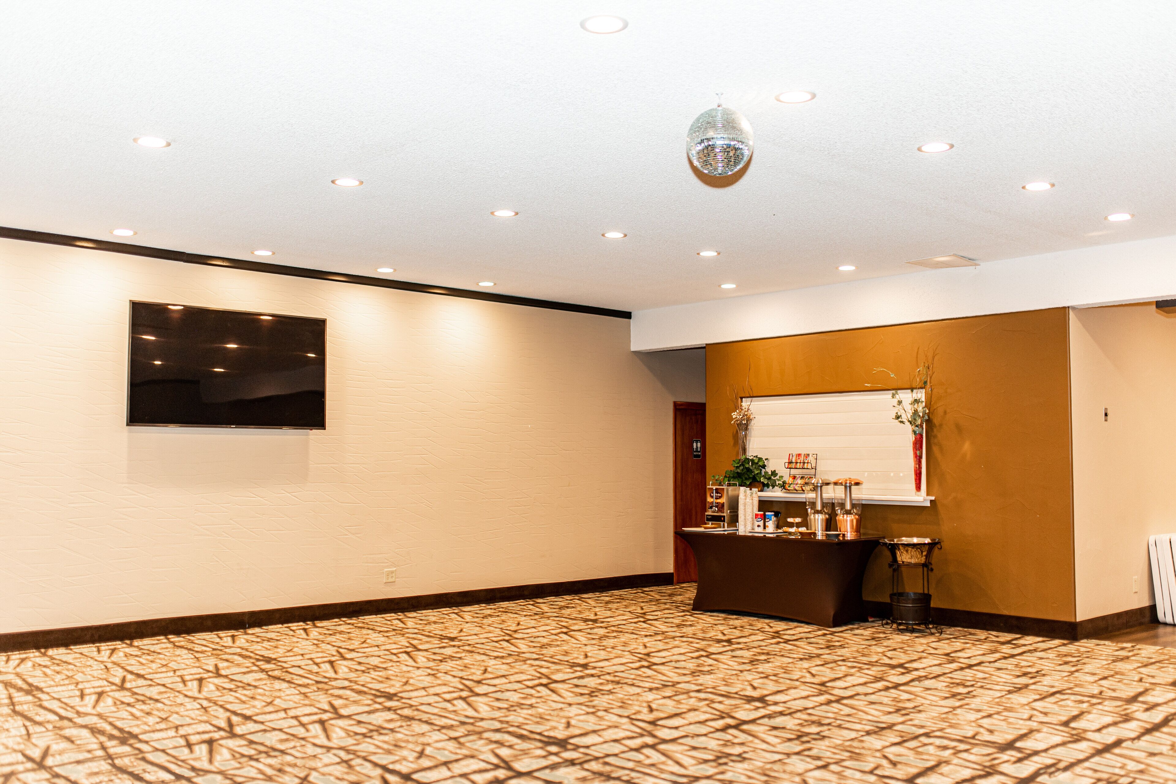 Hall d'albergo con tappeto a motivi, reception, televisore fissato al muro e illuminazione a incasso.