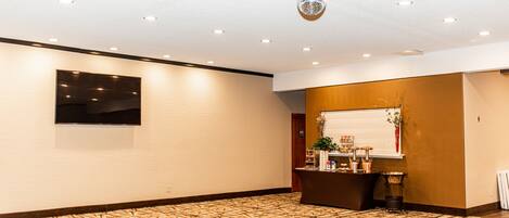 Hall d'albergo con tappeto a motivi, reception, televisore fissato al muro e illuminazione a incasso.