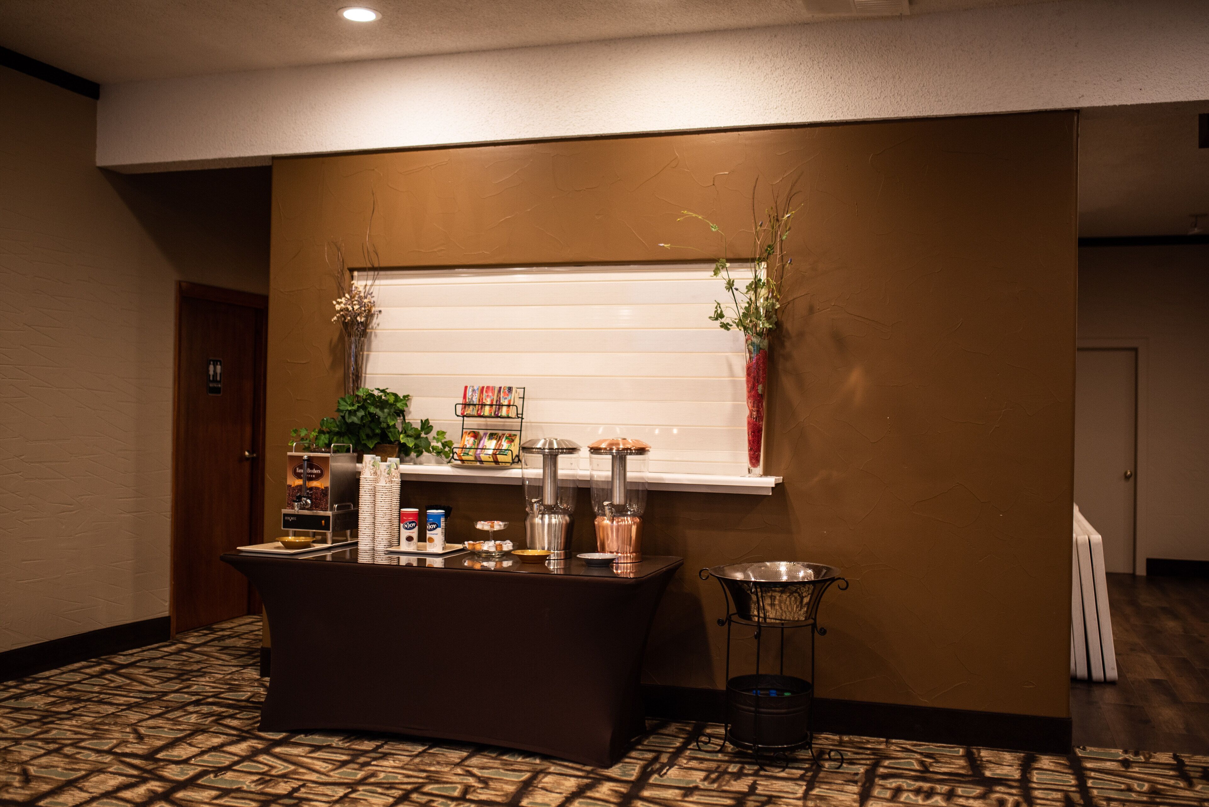 A reception area with a counter, a coffee machine, a plant, and a window with blinds.