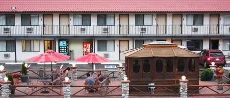 A motel with outdoor seating, a small wooden structure, and a red roof.