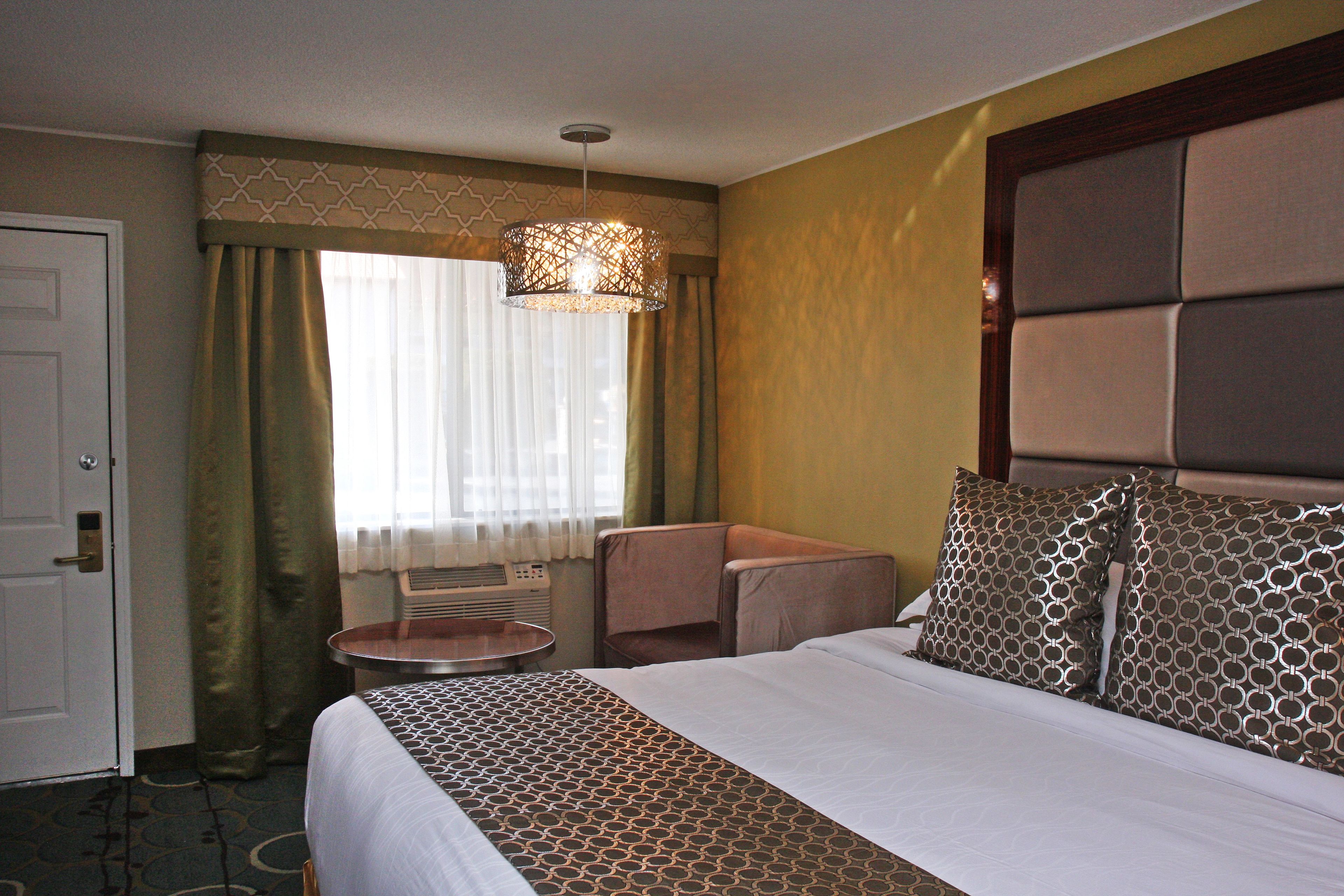 A hotel room with a large bed, a small round table, a chair, and a ceiling light fixture.
