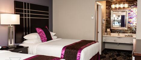 A hotel room with two beds, a nightstand, a lamp, a mirror, and a bathroom with a vanity.