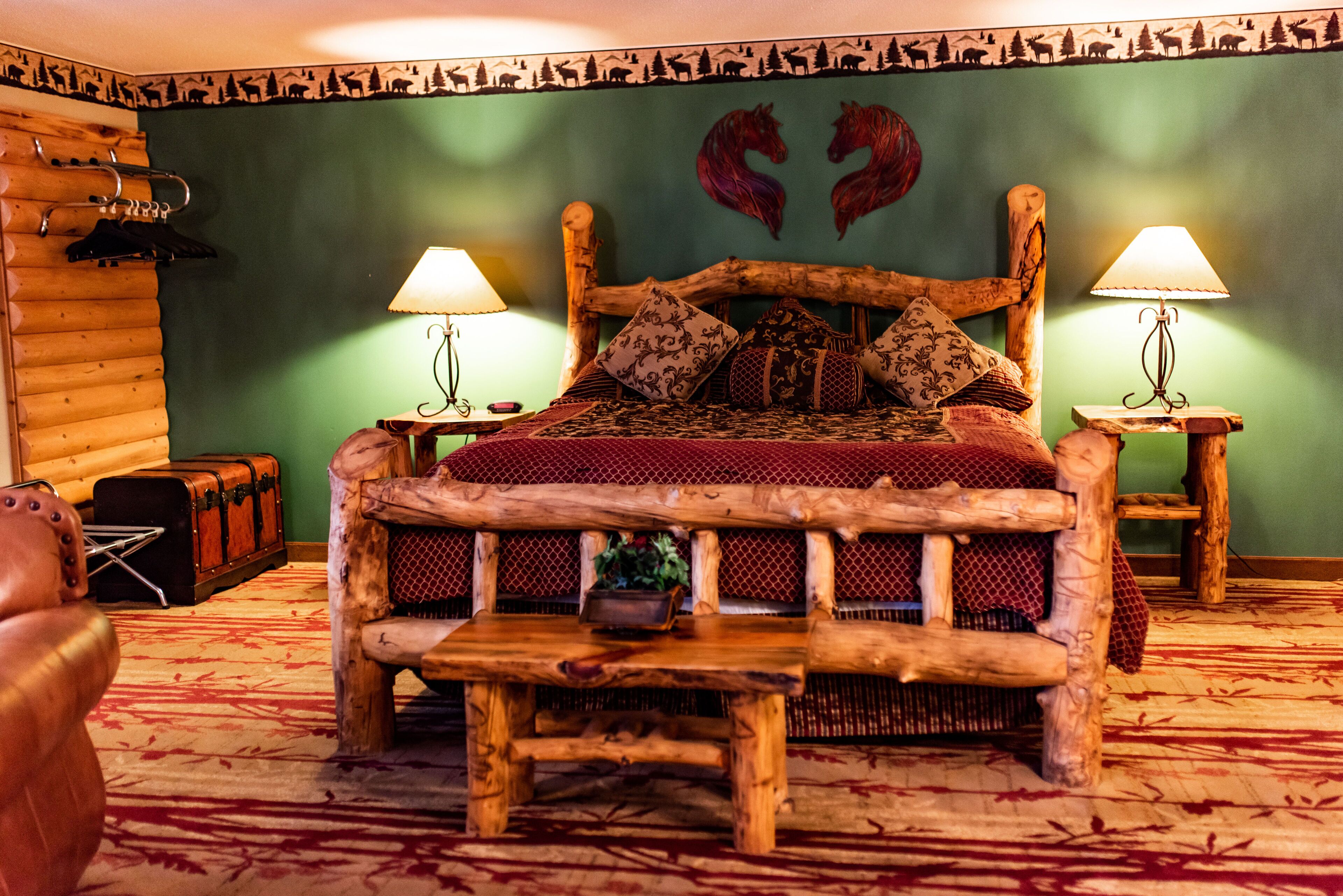A rustic wooden bed with a bench, two bedside lamps, and a decorative wall with animal silhouettes.