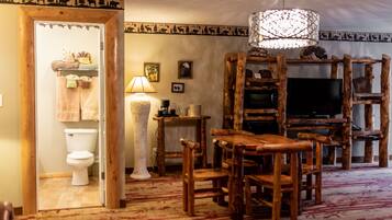 A rustic interior with a wooden dining table, chairs, a television, and a decorative lamp.