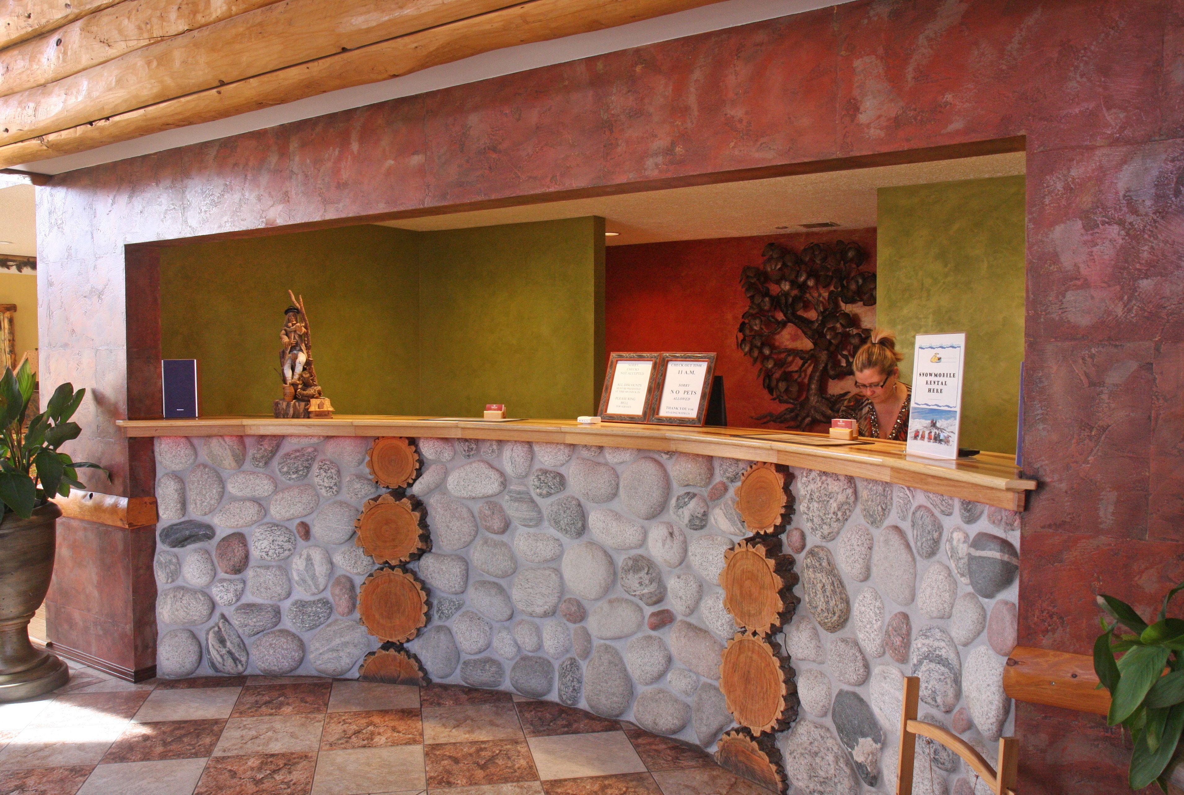 Un mostrador de recepción con diseño de piedra y madera, una planta en maceta y un cartel.