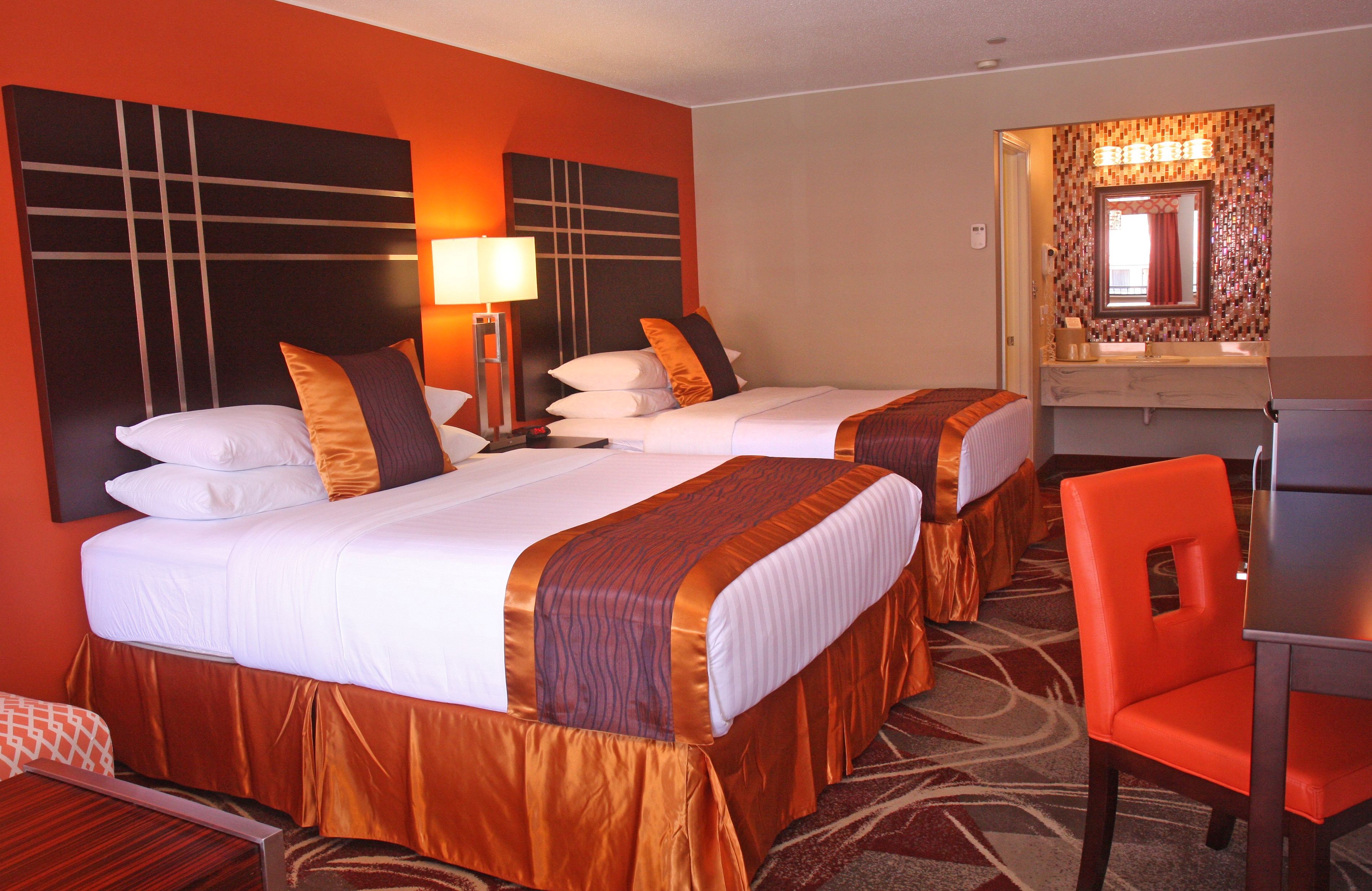 Ein Hotelzimmer mit zwei Betten, einem Schreibtisch, einem Stuhl und einem Badezimmer mit Spiegel.