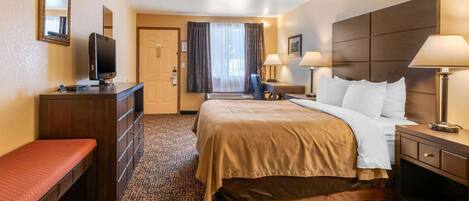 A hotel room with a bed, bedside tables, a desk, a TV, a bench, and a carpeted floor.