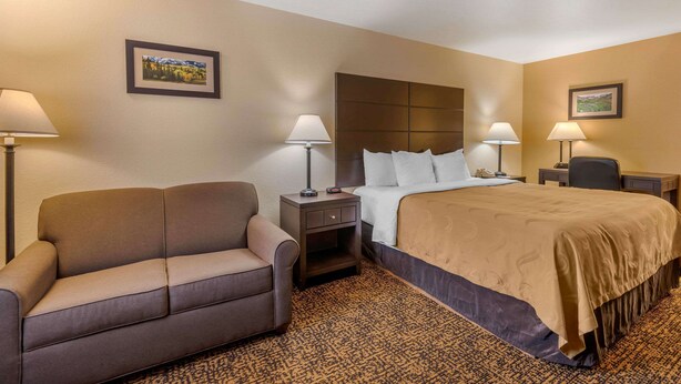 A hotel room with a bed, a sofa, two bedside tables with lamps, and a carpeted floor. - Quality Inn Ouray (Ouray)