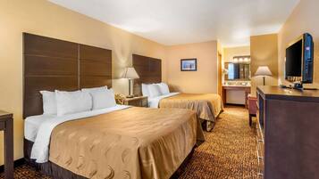 A hotel room with two beds, a desk, a TV, and a bathroom with a mirror and sink.