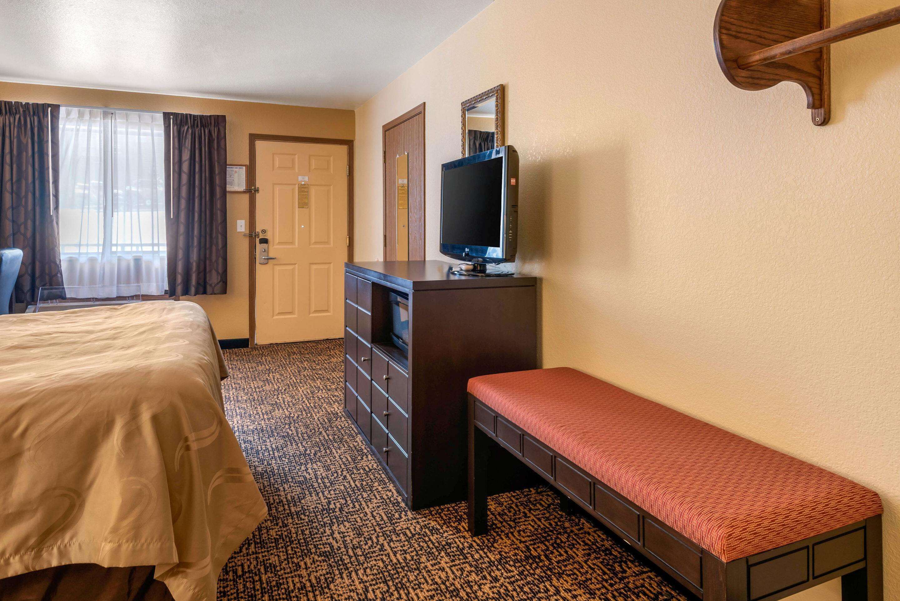 A hotel room with a bed, a bench, a dresser, a television, and a door.