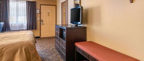 A hotel room with a bed, a bench, a dresser, a television, and a door.