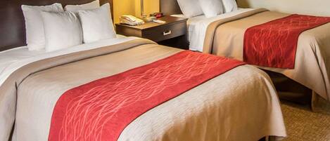 A hotel room with two beds, each with a red and beige bedspread, a nightstand with a lamp, a phone, and a clock.