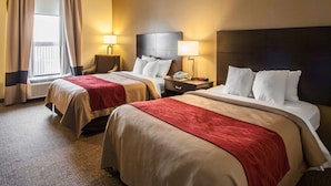 A hotel room with two beds, a window with curtains, a chair, and bedside tables with lamps. - Quality Inn Hayti North (Hayti)