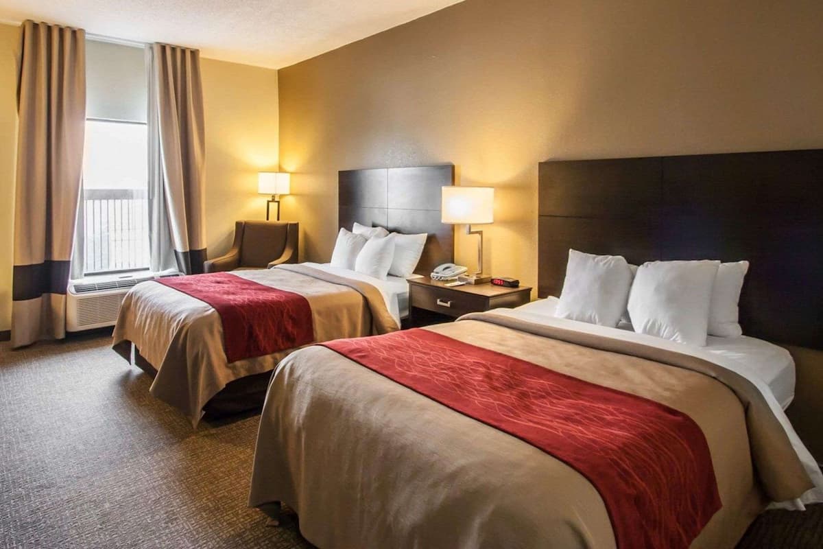 A hotel room with two beds, a window with curtains, a chair, and bedside tables with lamps.