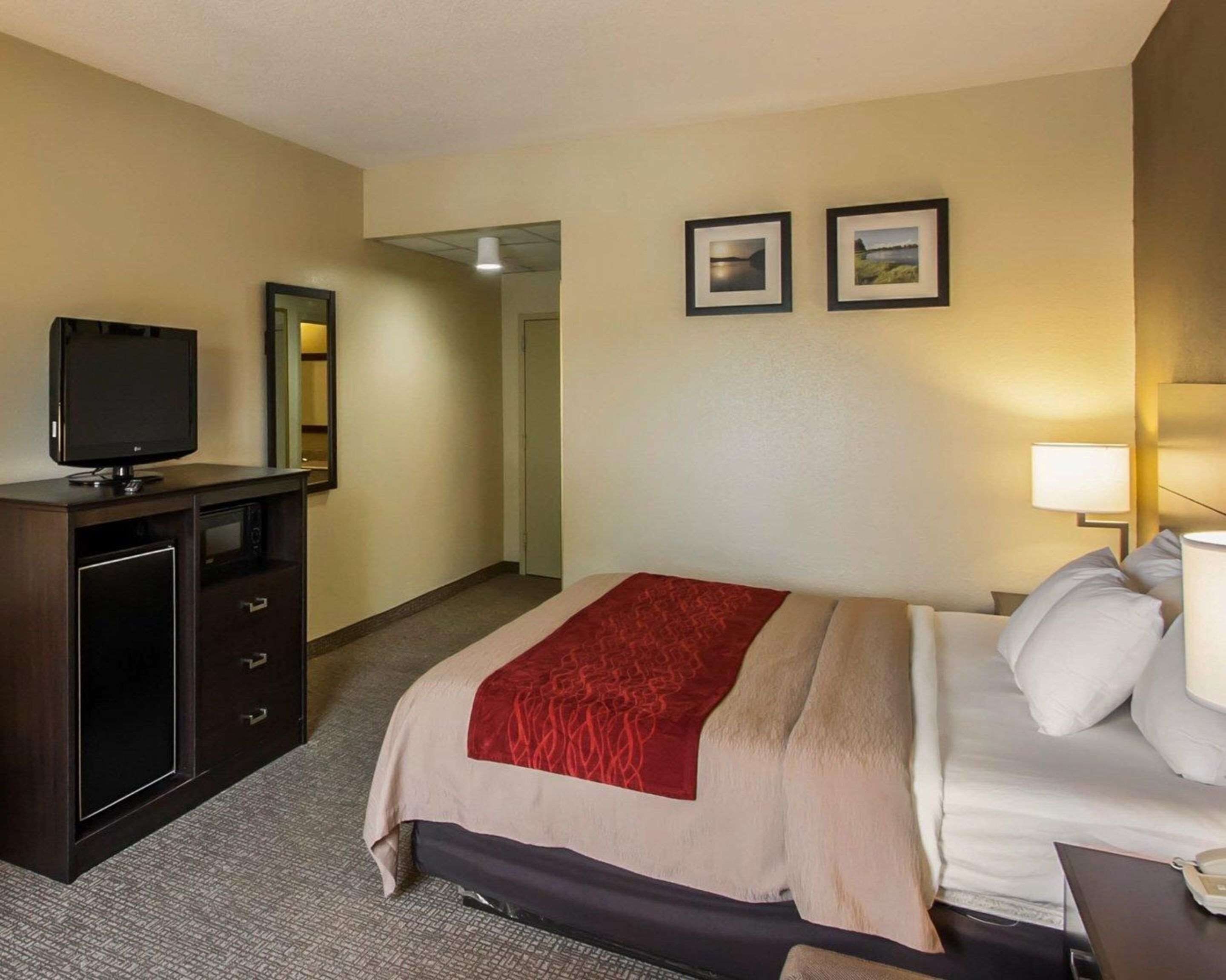 A hotel room with a bed, a TV, a desk with drawers, and two framed pictures on the wall.
