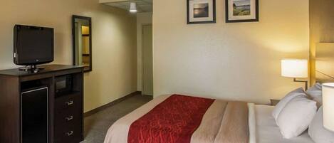 A hotel room with a bed, a TV, a desk with drawers, and two framed pictures on the wall.