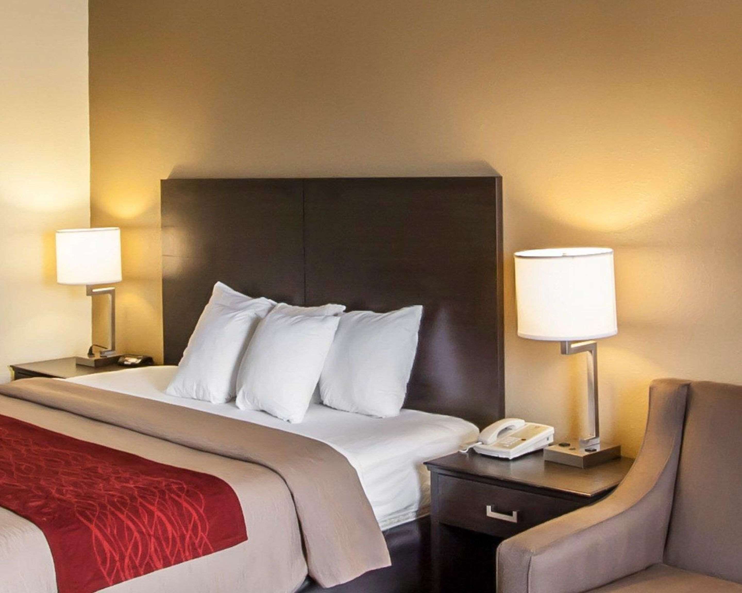 A hotel room with a large bed, two bedside lamps, a bedside phone, and a chair.