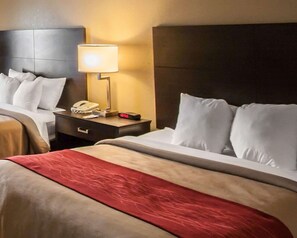 A hotel room with two beds, a nightstand with a lamp, a phone, and a digital clock.