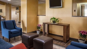 A lobby with a reception desk, a flat-screen TV, seating area with chairs and ottomans, and potted plants. - Quality Inn Hayti North (Hayti)