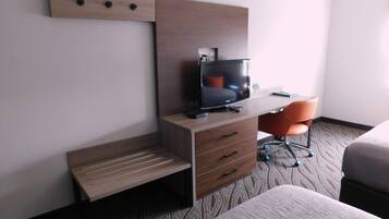 A hotel room with a wooden desk, a television, a chair, and a bed.