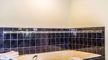 A bathroom with a bathtub, dark blue tiles, and a white towel on the side.