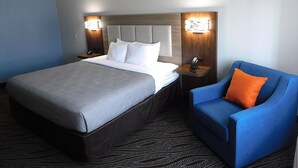 A hotel room with a large bed, two bedside tables with lamps, a blue armchair, and a patterned carpet. - Quality Inn Pontiac (Pontiac)