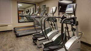 Un gimnasio con cintas de correr, elípticas y un espejo grande.