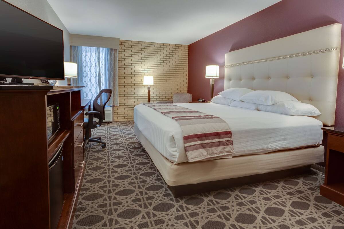 Una habitación de hotel con una cama grande, televisión, escritorio con computadora y una silla.
