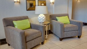 Dos sillones grises con cojines verdes, una mesita auxiliar con una lámpara blanca y apliques de pared.