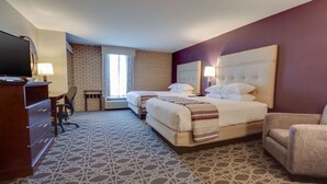 Habitación de hotel con pared de ladrillo, dos camas, un escritorio y un televisor, y una alfombra estampada.