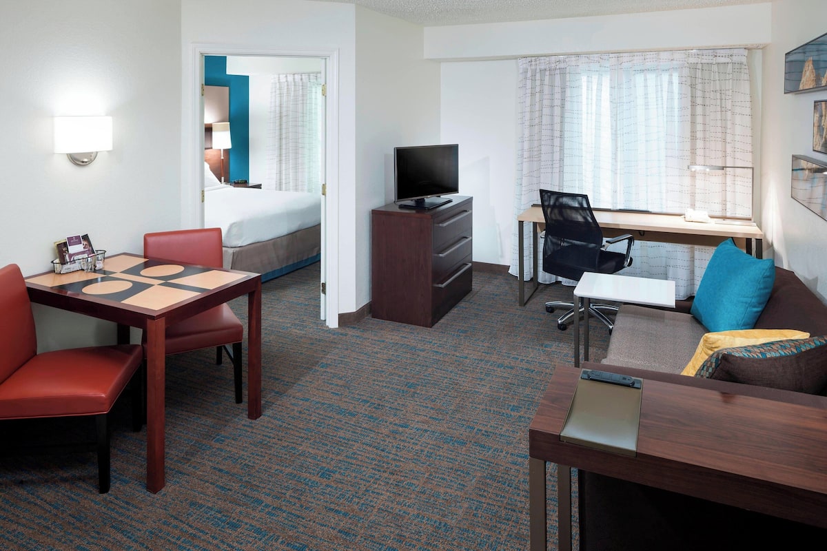 A hotel room with a bed, a desk with a computer, a TV, a dining table with chairs, and a sofa.