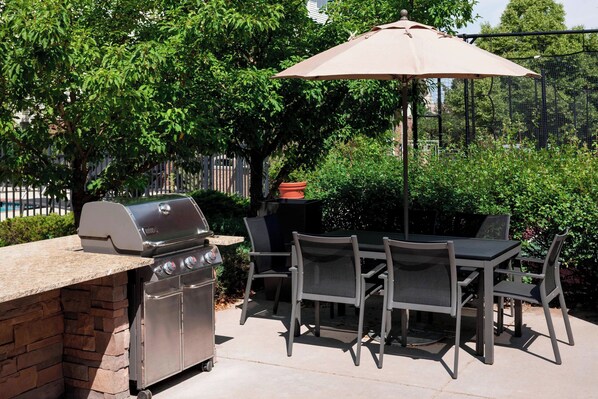 An outdoor patio with a grill, table, chairs, and a large umbrella.