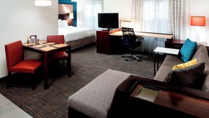 A hotel room with a bed, a desk with a TV, a sofa, and a dining table with chairs.
