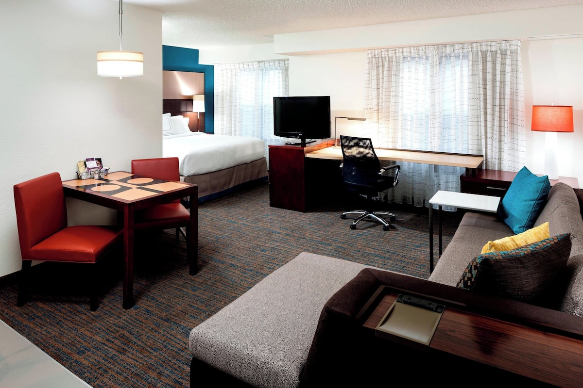 A hotel room with a bed, a desk with a TV, a sofa, and a dining table with chairs.