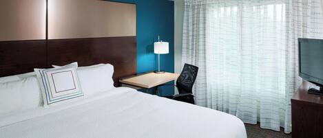 A hotel room with a large bed, a desk with a lamp, a television, and a window with curtains.