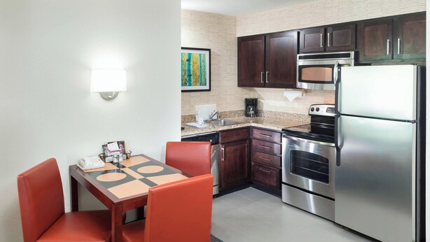 A compact kitchen with a dining table, chairs, a refrigerator, oven, microwave, and a coffee maker.