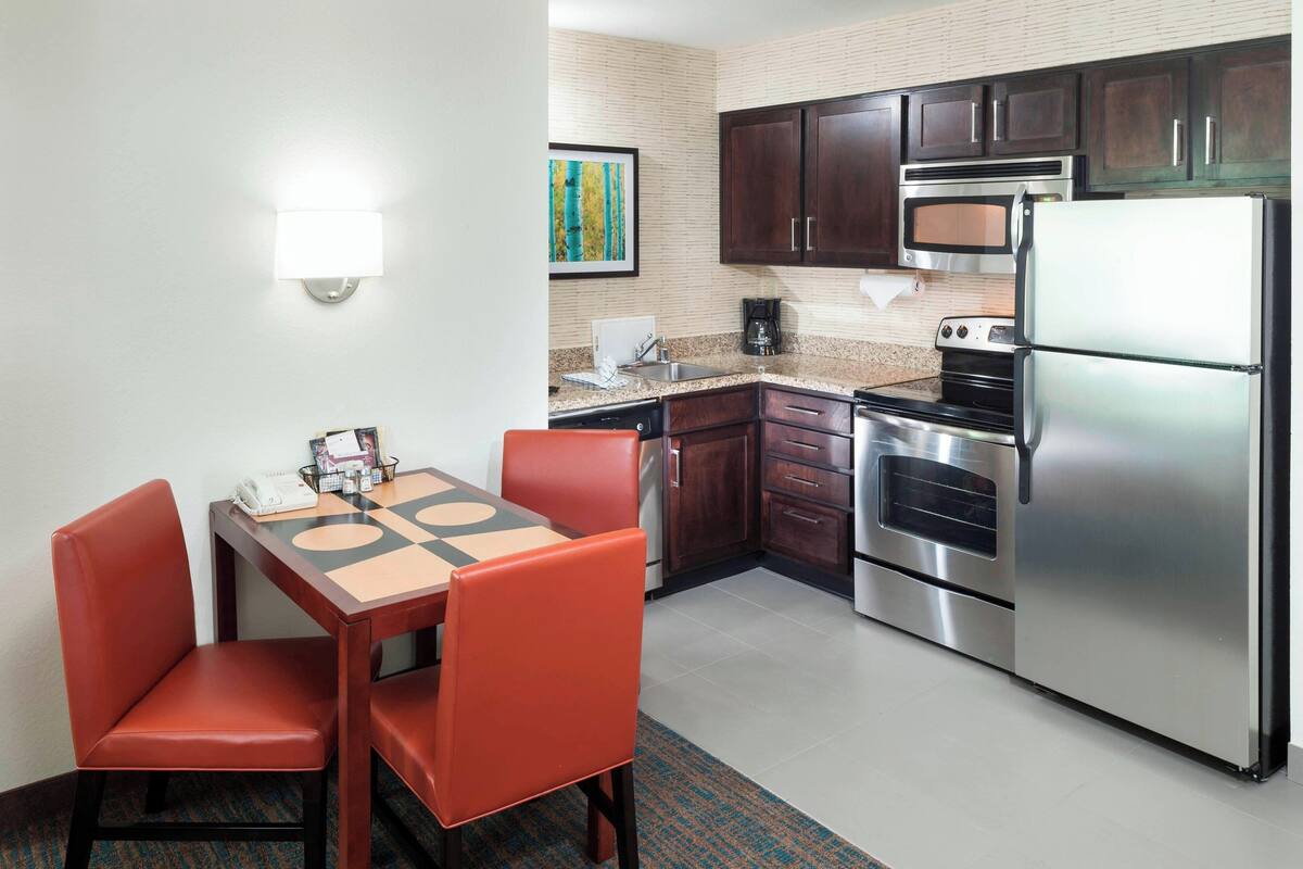 A compact kitchen with a dining table, chairs, a refrigerator, oven, microwave, and a coffee maker.