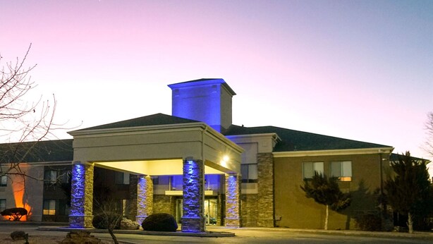 Entrada de hotel con zona cubierta, pilares de piedra y una chimenea iluminada de azul.