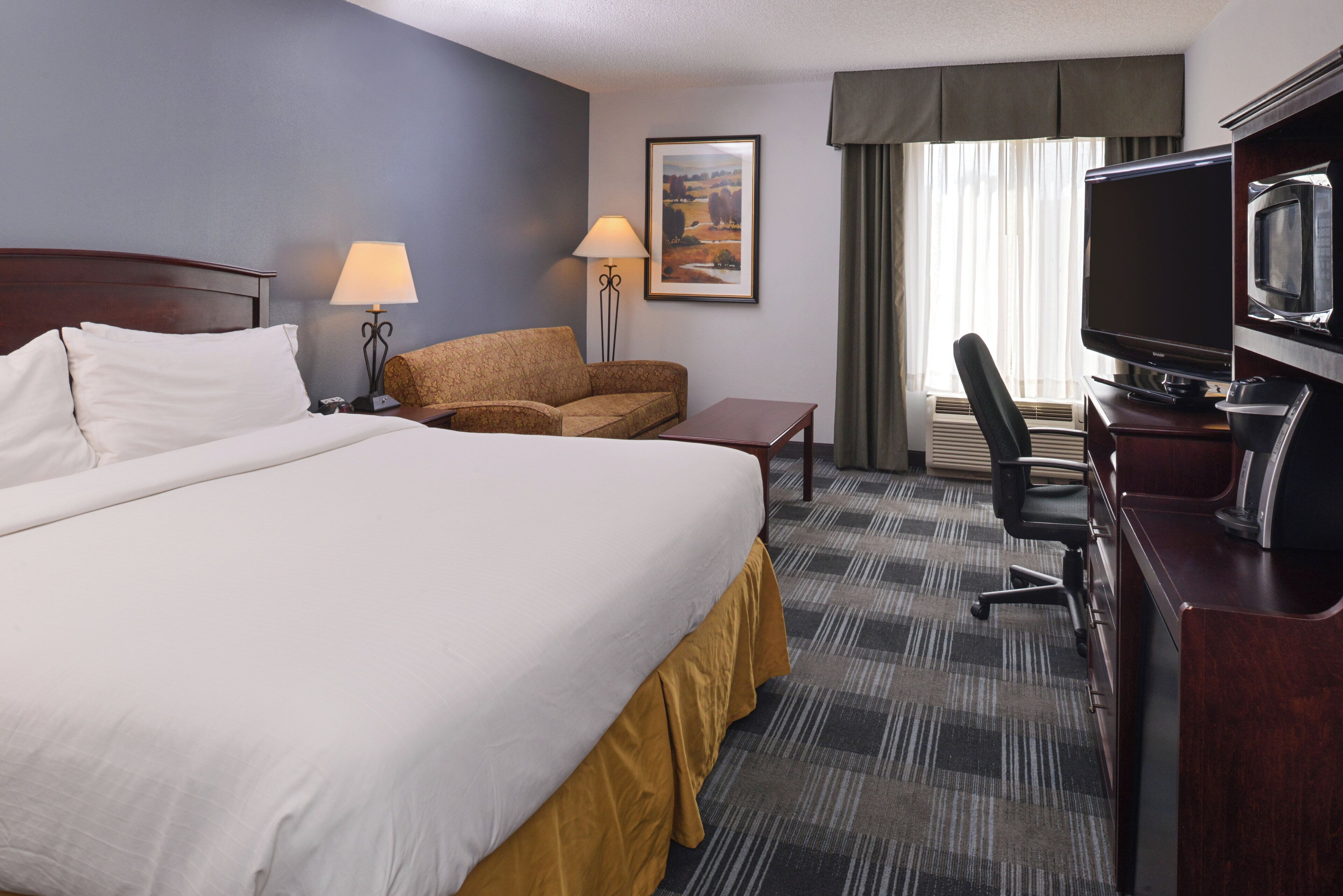 A hotel room with a bed, a desk, a chair, a television, and a lamp.