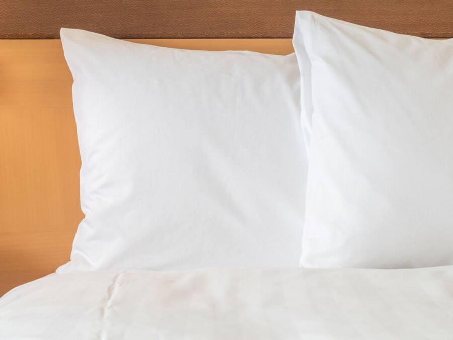 A bed with white bedding and pillows against a wooden headboard.