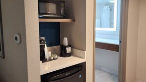 Una kitchenette compacta con microondas, cafetera y refrigerador pequeño.