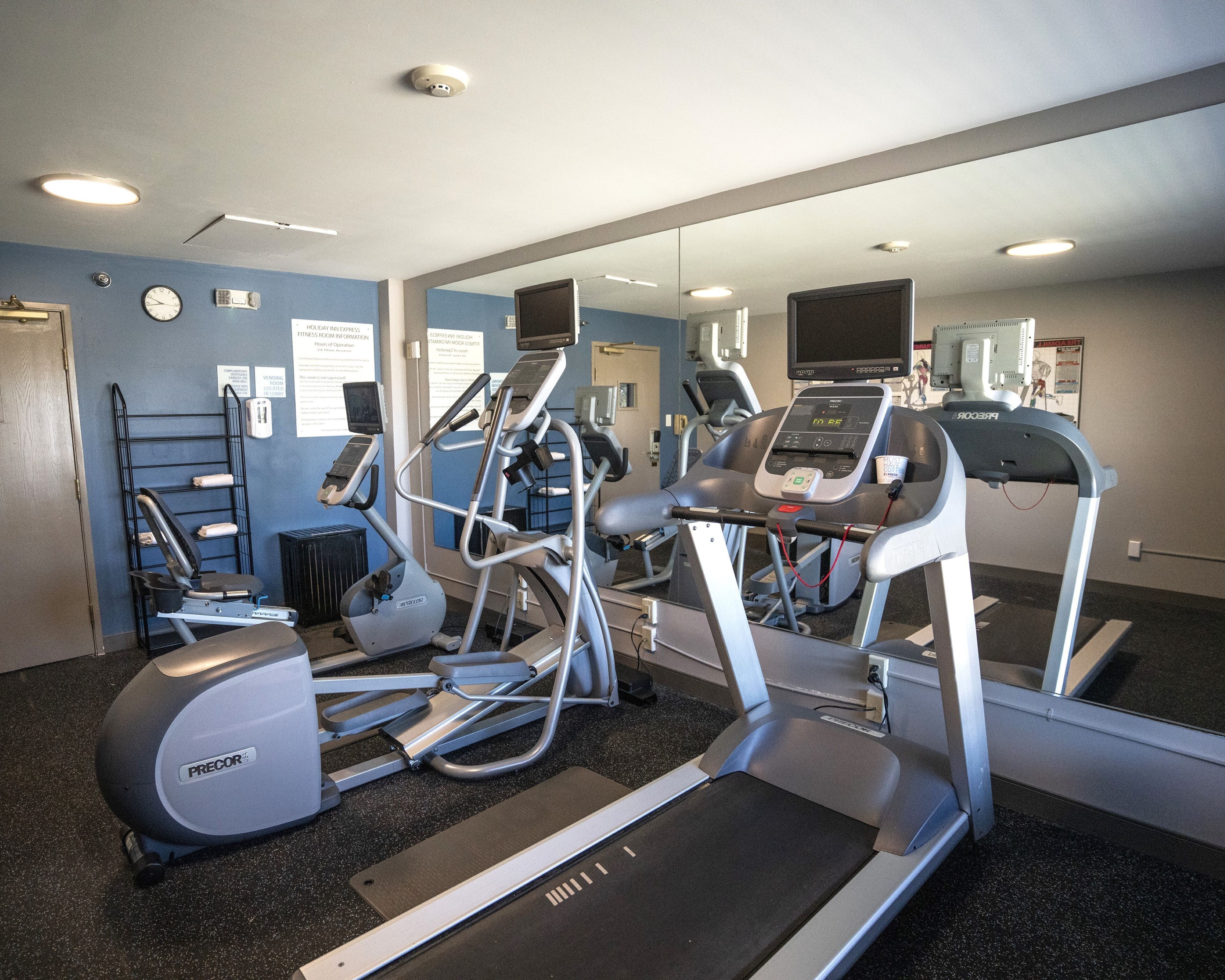 A gym with treadmills, ellipticals, and a mirrored wall.