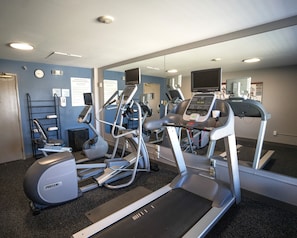 A gym with treadmills, ellipticals, and a mirrored wall.
