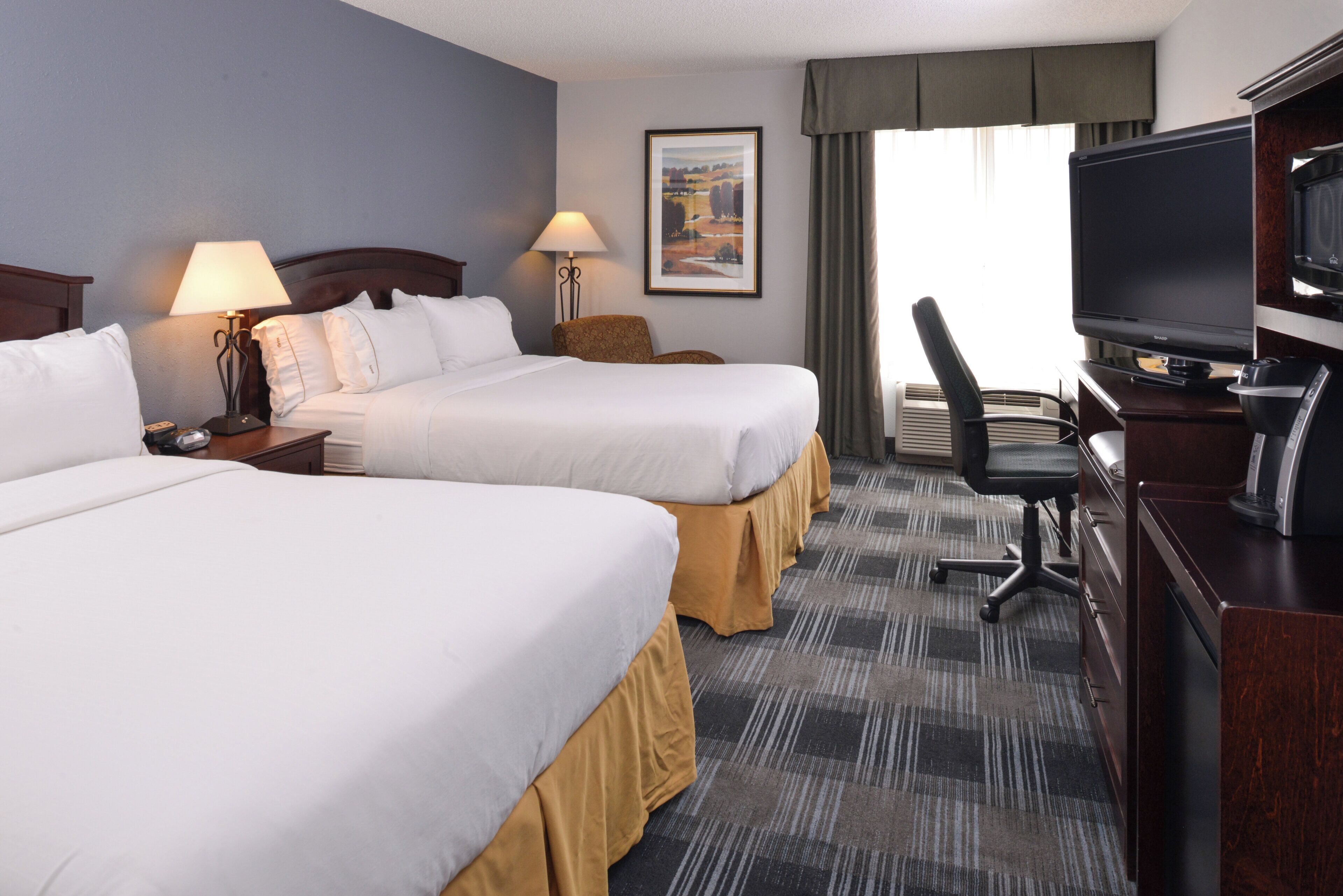 A hotel room with two beds, a desk with a television, and a chair.